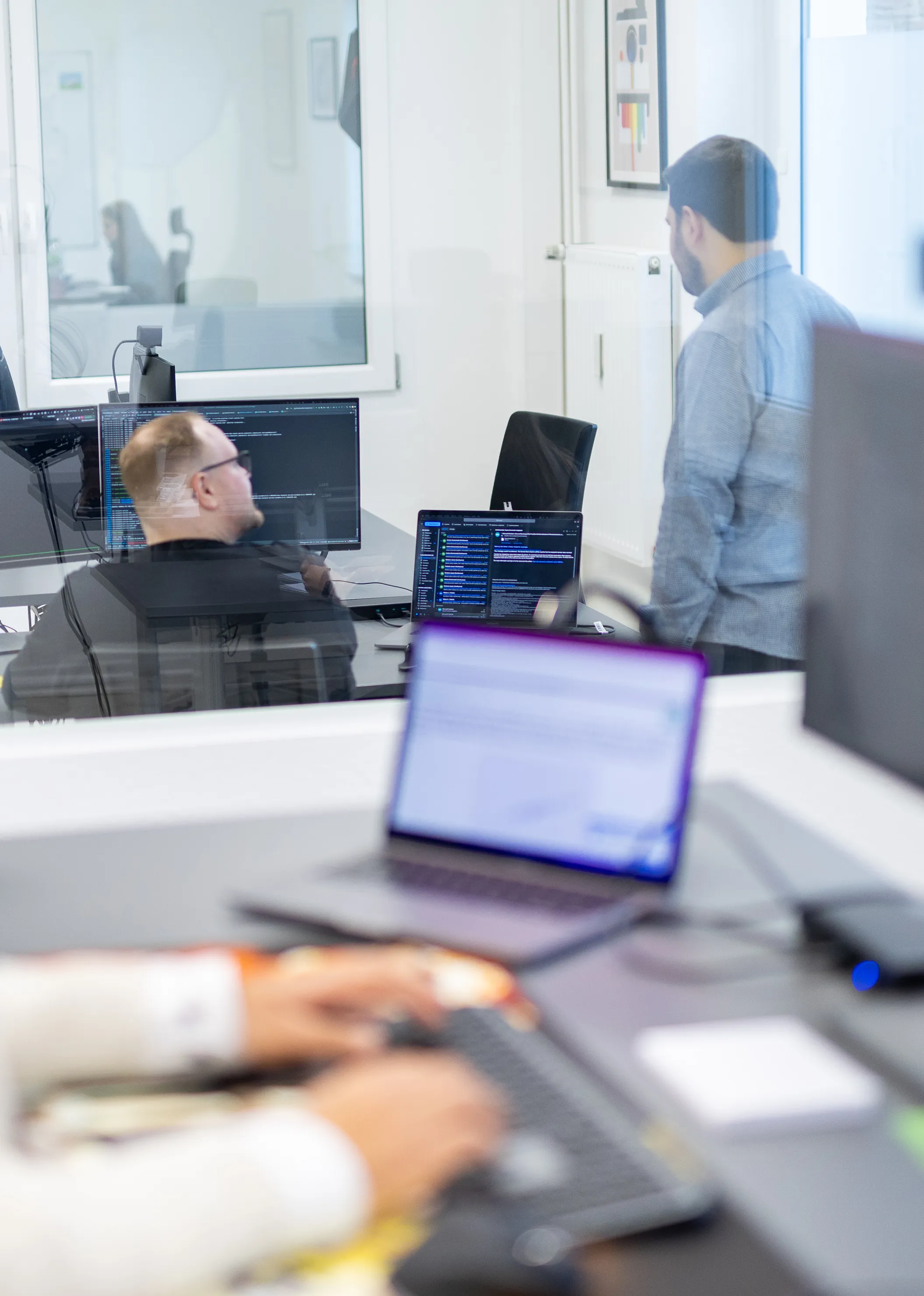 Modernes Büro mit Personen die am Computer arbeiten. Zwei Personen führen ein Gespräch am Schreibtisch.